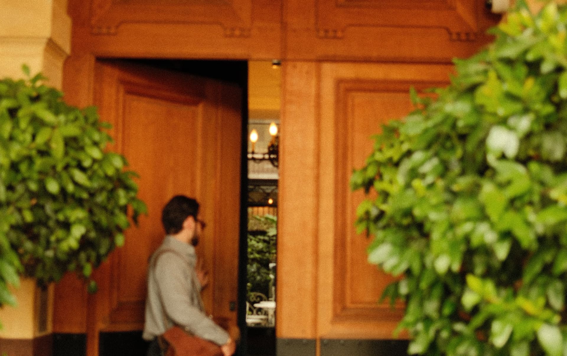 A guest stepping through a grand wooden doorway into a warmly lit hotel lobby